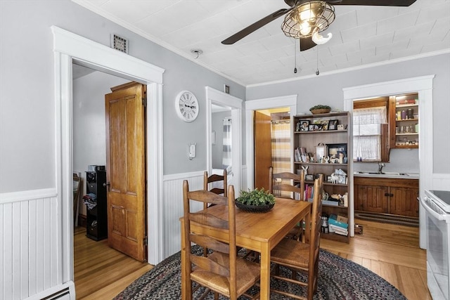 dining area featuring a baseboard heating unit, a ceiling fan, light wood finished floors, and wainscoting