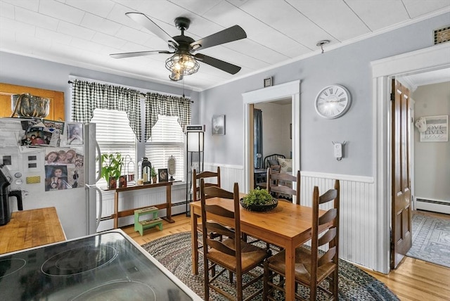 dining area with a ceiling fan, ornamental molding, wainscoting, and light wood finished floors