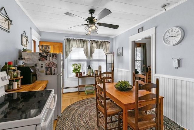 dining room with light wood-style floors, a wainscoted wall, and ceiling fan