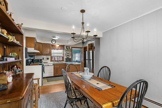 dining space with a baseboard radiator, a notable chandelier, wood finished floors, and ornamental molding