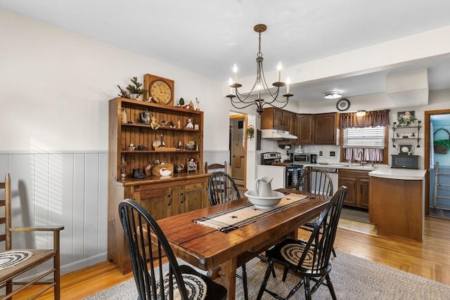 dining room featuring a wainscoted wall, light wood-style floors, and a chandelier