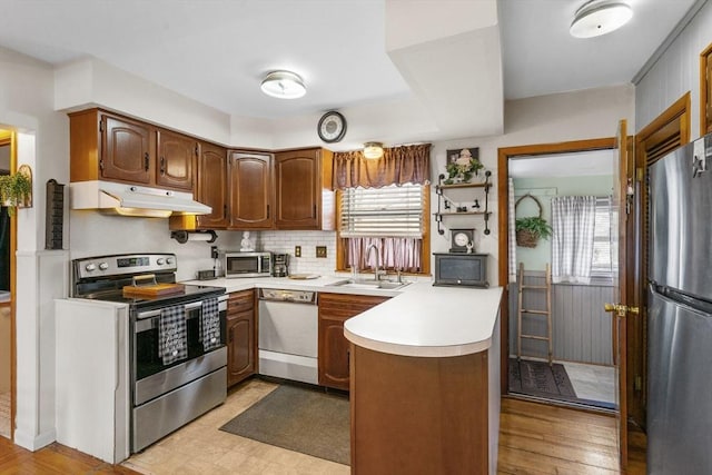 kitchen with a peninsula, a sink, light countertops, under cabinet range hood, and appliances with stainless steel finishes