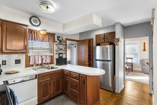 kitchen with a sink, freestanding refrigerator, a peninsula, light countertops, and dishwasher