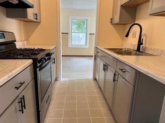 kitchen featuring gray cabinets, a sink, range hood, light tile patterned floors, and gas range