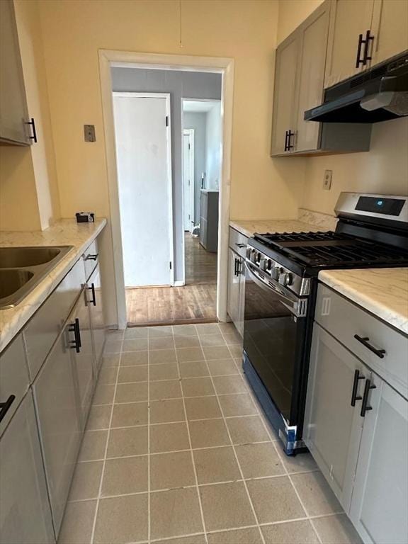 kitchen featuring light tile patterned floors, gray cabinets, a sink, under cabinet range hood, and stainless steel gas stove