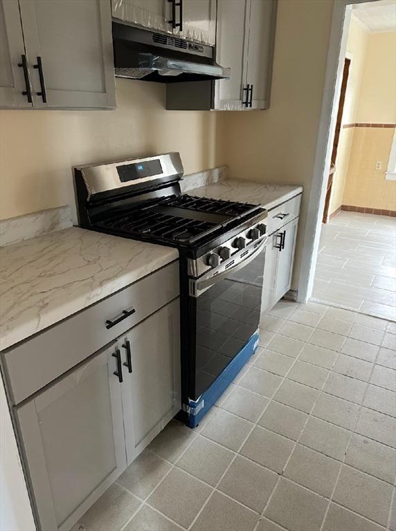 kitchen featuring light stone counters, light tile patterned flooring, gray cabinetry, under cabinet range hood, and gas range