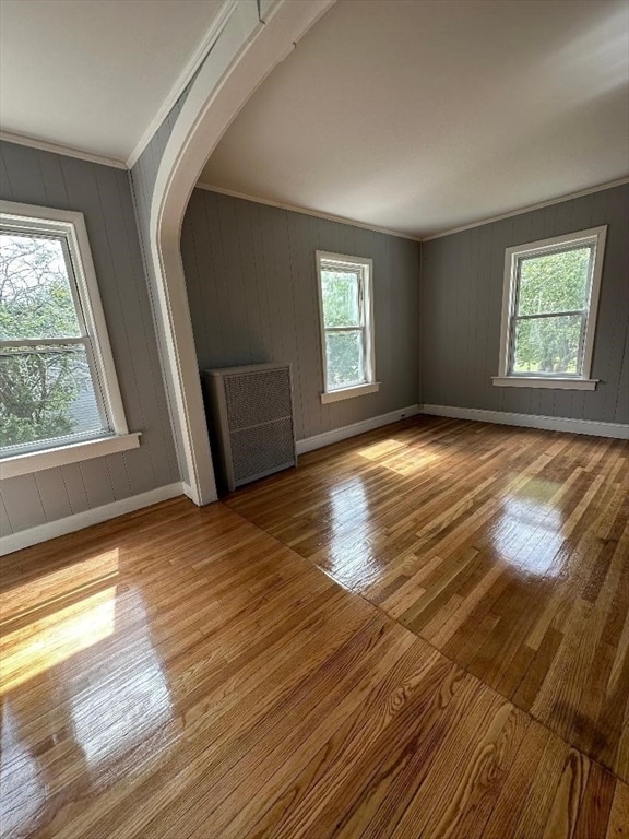 unfurnished living room featuring ornamental molding, radiator heating unit, wooden walls, and hardwood / wood-style flooring