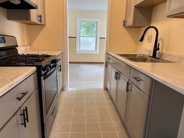 kitchen featuring a textured ceiling, stainless steel gas range oven, light tile patterned floors, range hood, and sink