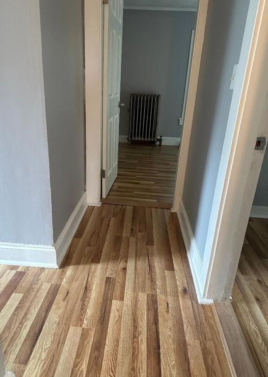 corridor with radiator, wood finished floors, and baseboards