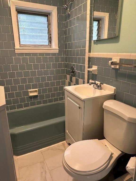 bathroom featuring vanity, washtub / shower combination, tile walls, toilet, and marble finish floor