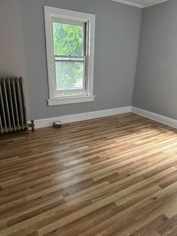 unfurnished room featuring radiator, wood finished floors, and baseboards