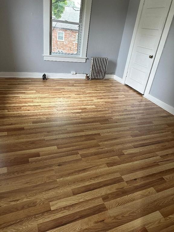 spare room with radiator heating unit, baseboards, and wood finished floors