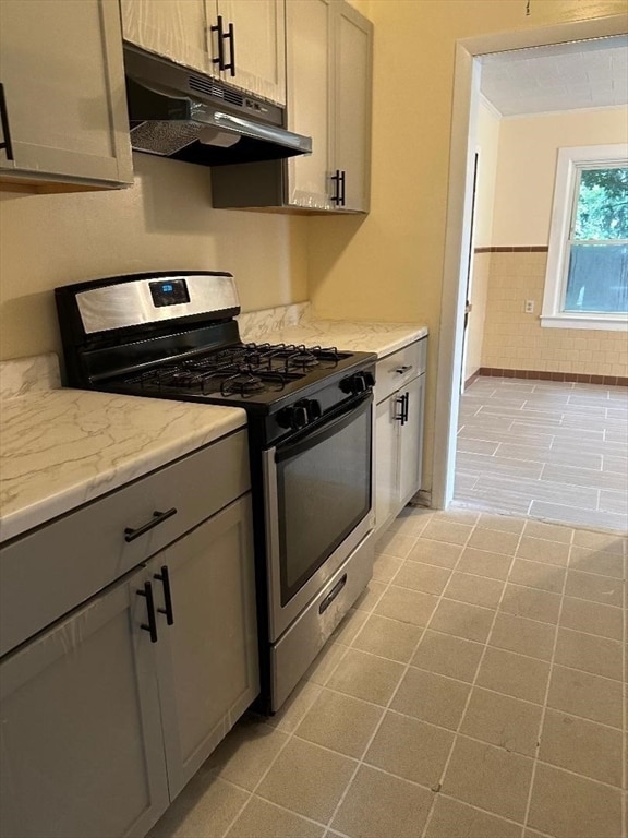 kitchen featuring light tile patterned floors, light stone counters, gray cabinets, and stainless steel gas range