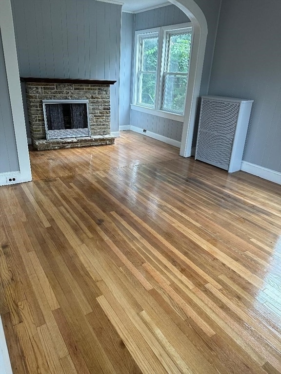 unfurnished living room with hardwood / wood-style floors, wooden walls, radiator, and a stone fireplace