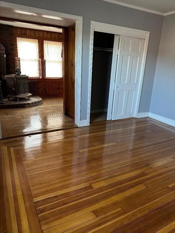 unfurnished bedroom with a closet, wood finished floors, a wood stove, and crown molding