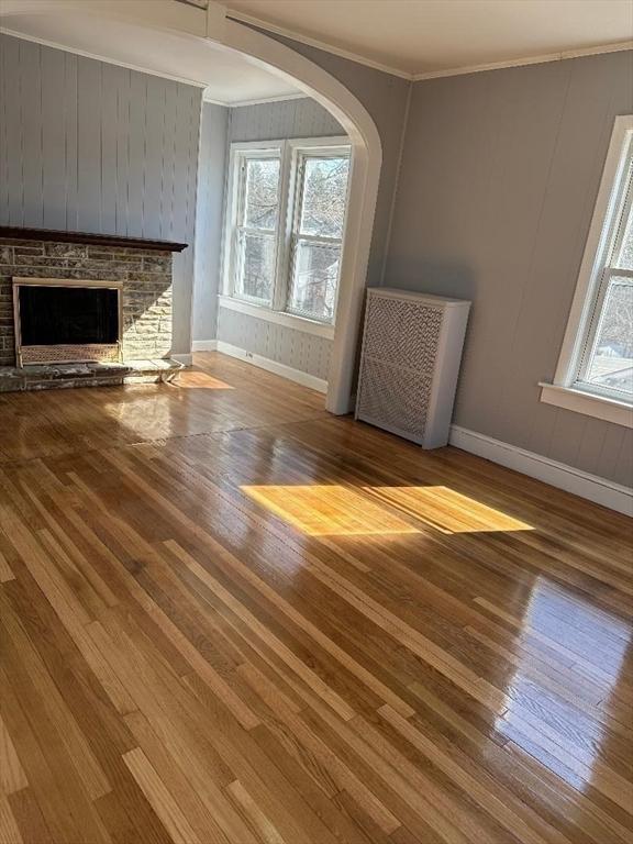 unfurnished living room with baseboards, a fireplace, hardwood / wood-style floors, and crown molding