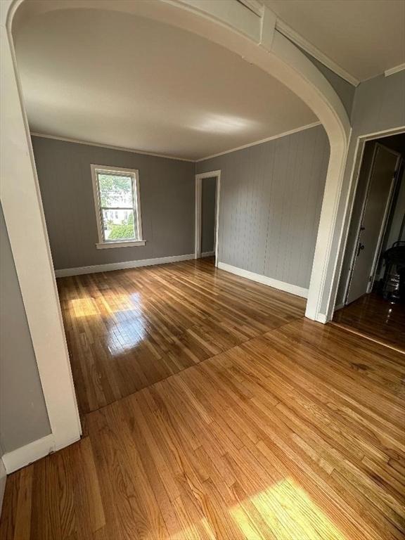 spare room with wood finished floors, baseboards, arched walkways, and ornamental molding