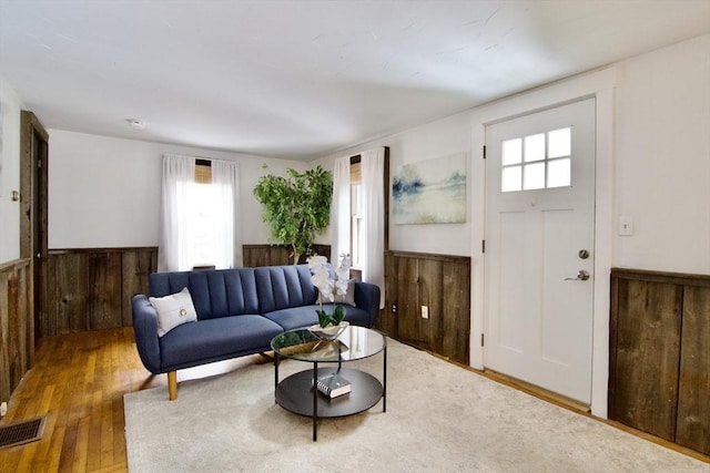 living room with a wainscoted wall, wooden walls, visible vents, and wood finished floors