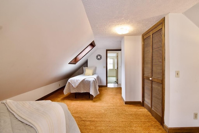 bedroom with a textured ceiling, lofted ceiling with skylight, a closet, and light carpet