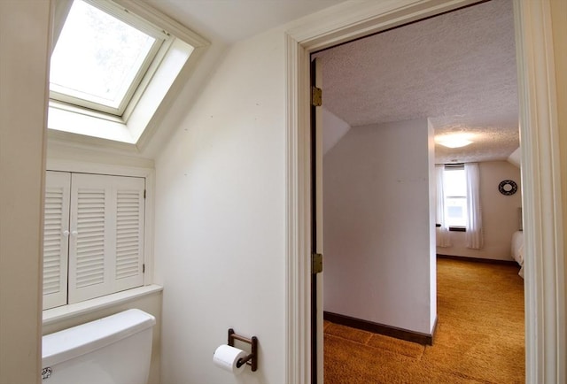 interior space featuring a textured ceiling, carpet floors, lofted ceiling with skylight, and baseboards