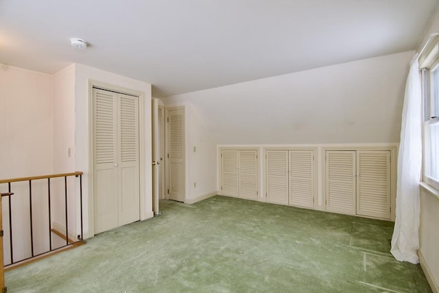 unfurnished bedroom featuring lofted ceiling, multiple windows, multiple closets, and light colored carpet