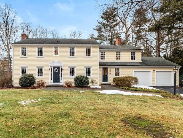 colonial house featuring a front lawn, an attached garage, driveway, and a chimney