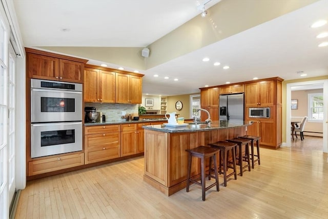 kitchen with light wood finished floors, backsplash, lofted ceiling, a kitchen breakfast bar, and appliances with stainless steel finishes