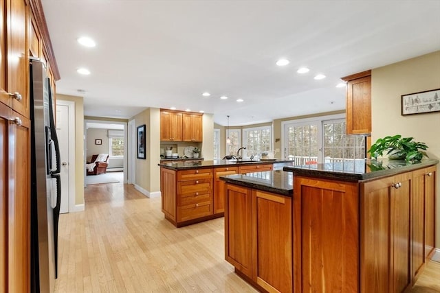 kitchen with light wood finished floors, dark stone counters, recessed lighting, brown cabinets, and a peninsula