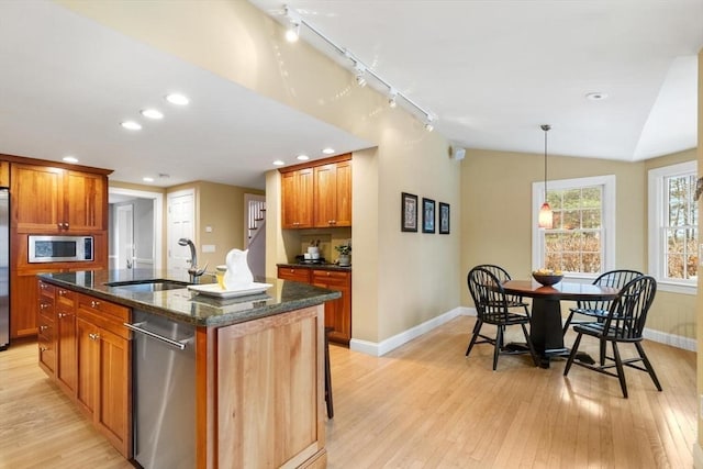 kitchen with a center island with sink, a sink, stainless steel appliances, light wood-style floors, and lofted ceiling