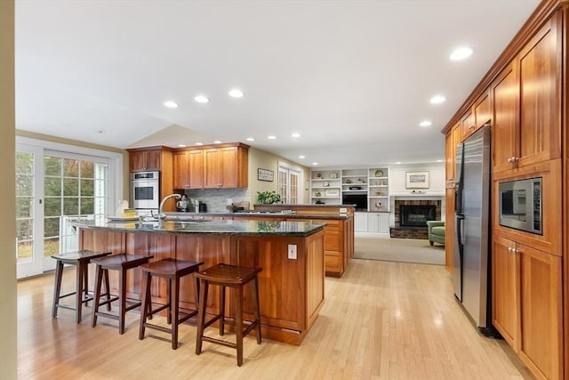 kitchen with brown cabinetry, a center island with sink, appliances with stainless steel finishes, and a breakfast bar