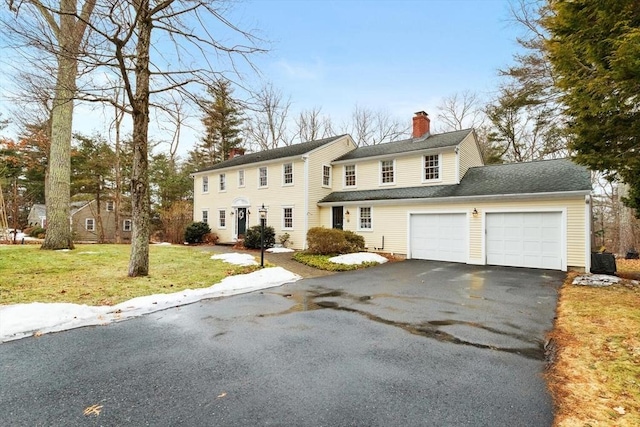 colonial inspired home featuring a garage, driveway, a chimney, and a front lawn