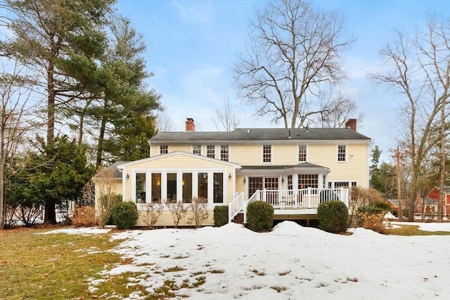 snow covered back of property featuring a wooden deck, a chimney, and a sunroom