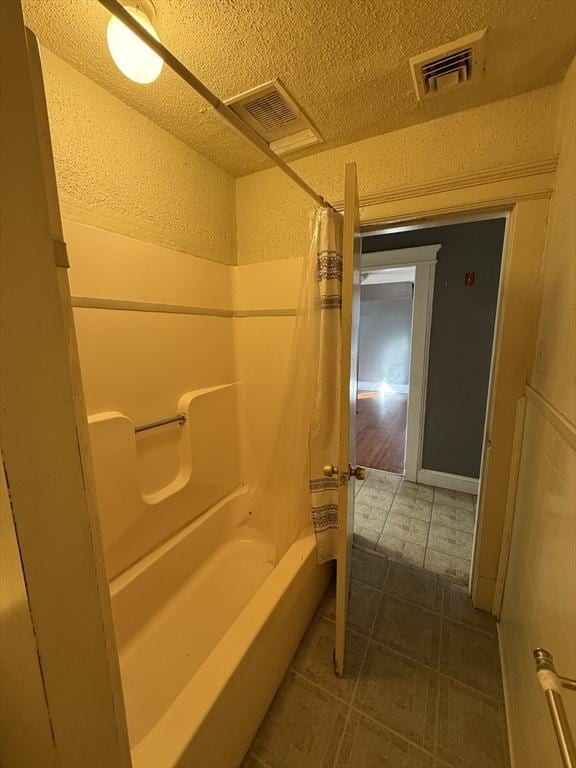 bathroom with shower / bathtub combination with curtain and a textured ceiling