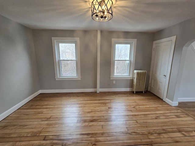 spare room featuring radiator, an inviting chandelier, a healthy amount of sunlight, and light hardwood / wood-style flooring