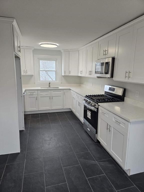 kitchen with dark tile patterned flooring, sink, white cabinetry, and stainless steel appliances