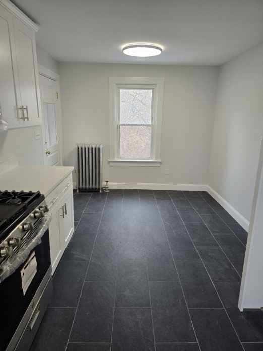 kitchen with white cabinetry, radiator heating unit, and stainless steel range with gas stovetop