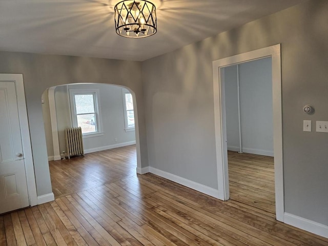 spare room featuring light hardwood / wood-style floors, radiator heating unit, and an inviting chandelier