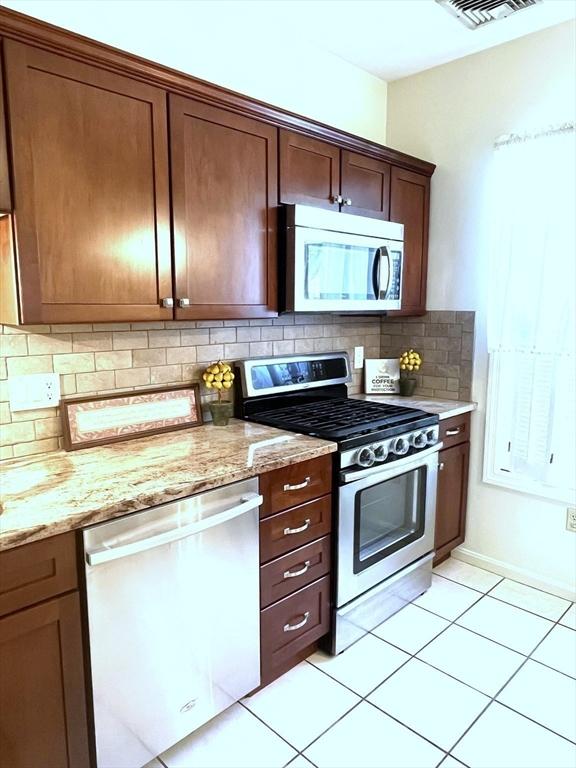 38 Hammond Pl Unit 38, Woburn, MA 01801 - kitchen featuring stainless steel appliances, decorative backsplash, light tile patterned floors, and light stone countertops