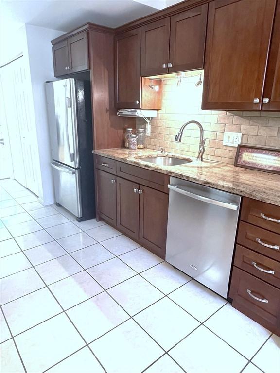 38 Hammond Pl Unit 38, Woburn, MA 01801 - kitchen with stainless steel appliances, light tile patterned flooring, decorative backsplash, light stone counters, and dark brown cabinetry