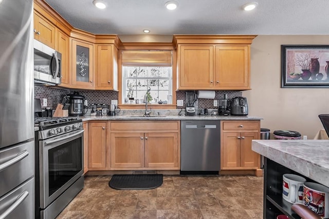 kitchen with stainless steel appliances, light stone countertops, sink, and backsplash