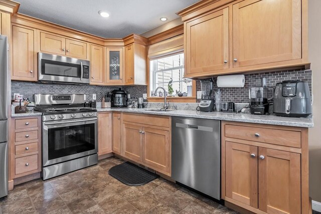 kitchen featuring light stone counters, appliances with stainless steel finishes, sink, and tasteful backsplash