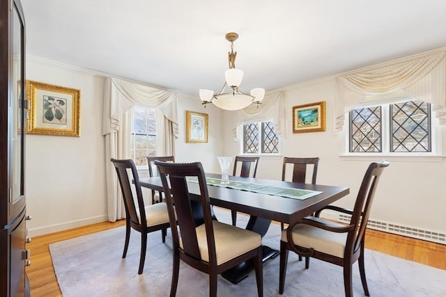 dining area with a baseboard radiator, an inviting chandelier, light wood-style floors, ornamental molding, and baseboards