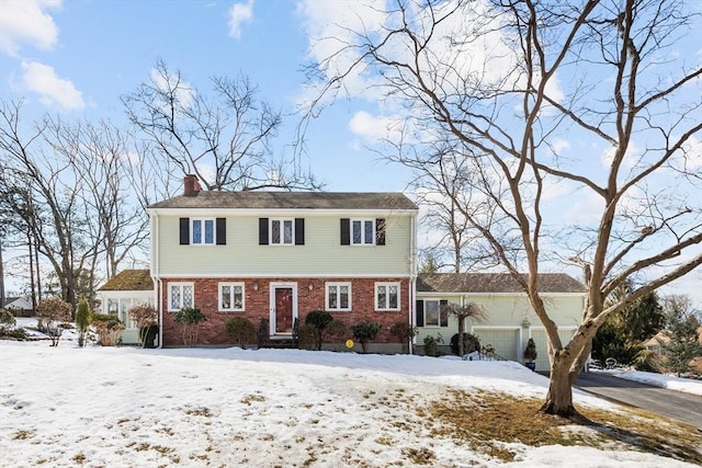 colonial house featuring a garage, driveway, a chimney, and brick siding