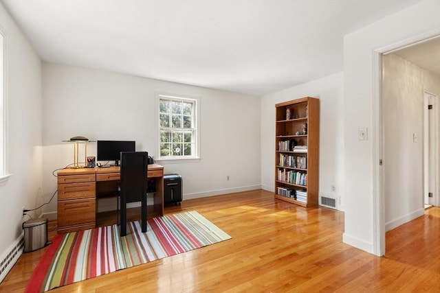 home office featuring a baseboard heating unit, visible vents, baseboards, and wood finished floors