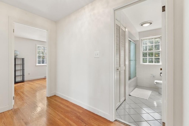 bathroom featuring baseboards, toilet, wood finished floors, combined bath / shower with glass door, and tile walls