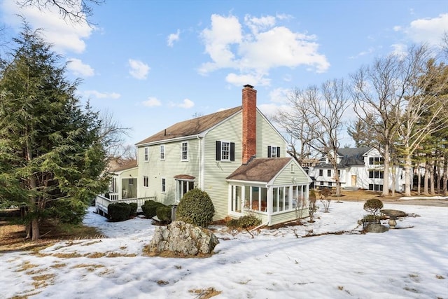 snow covered rear of property with a chimney and a sunroom