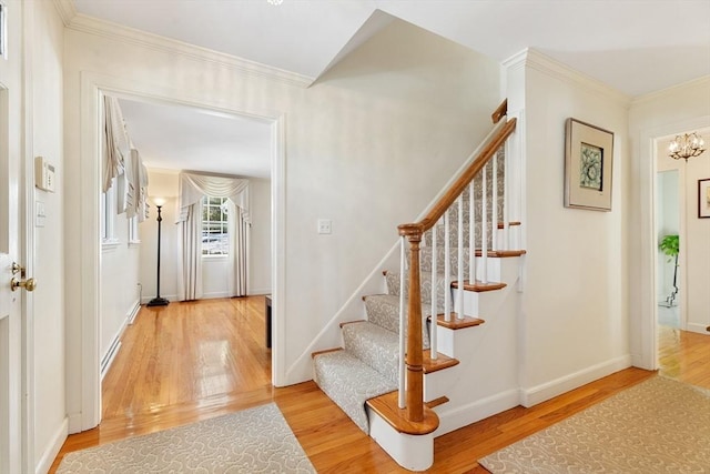 staircase featuring baseboards, ornamental molding, a chandelier, and wood finished floors