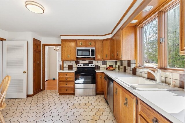 kitchen with brown cabinets, stainless steel appliances, light countertops, backsplash, and a sink