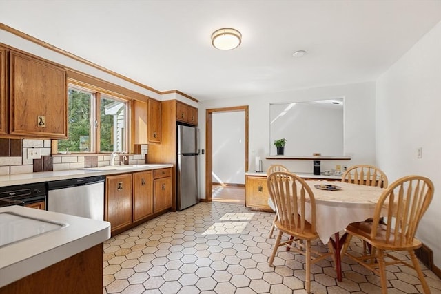 kitchen with a sink, light countertops, appliances with stainless steel finishes, backsplash, and brown cabinetry