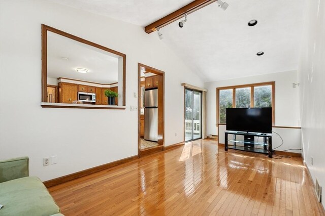 living room featuring track lighting, baseboards, lofted ceiling with beams, and light wood finished floors